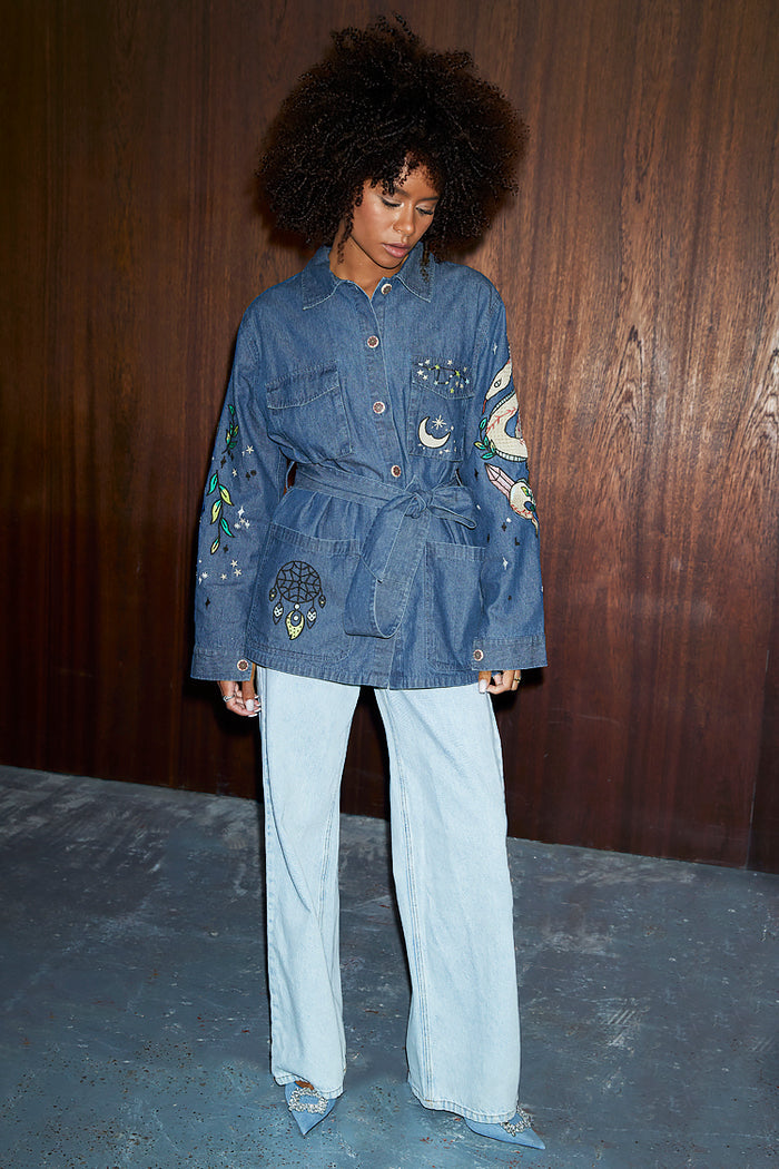 Blue Denim Manifestation Jacket featuring a tie waist and tarot motifs, paired with light-wash jeans.