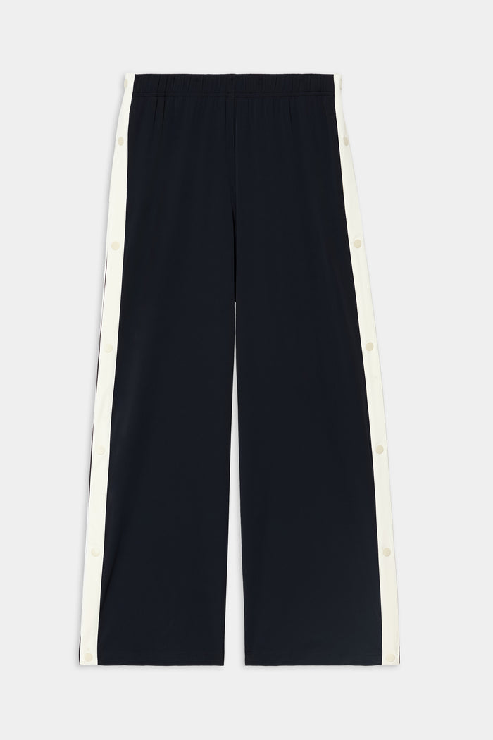 The SPLITS59 Jordan Nylon Twill Tearaway pants in Black/Creme are wide-leg pants crafted from a nylon-spandex blend, featuring white snap button panels running down the sides, and are displayed flat against a white background.