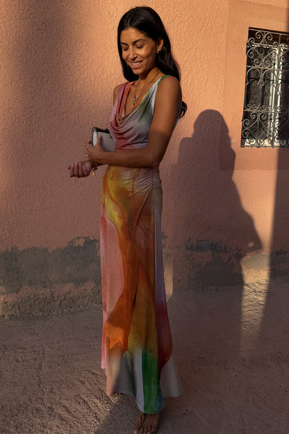 Abstract Malika Dress with a multicoloured print and draped neckline, styled on a model against a textured pink wall.