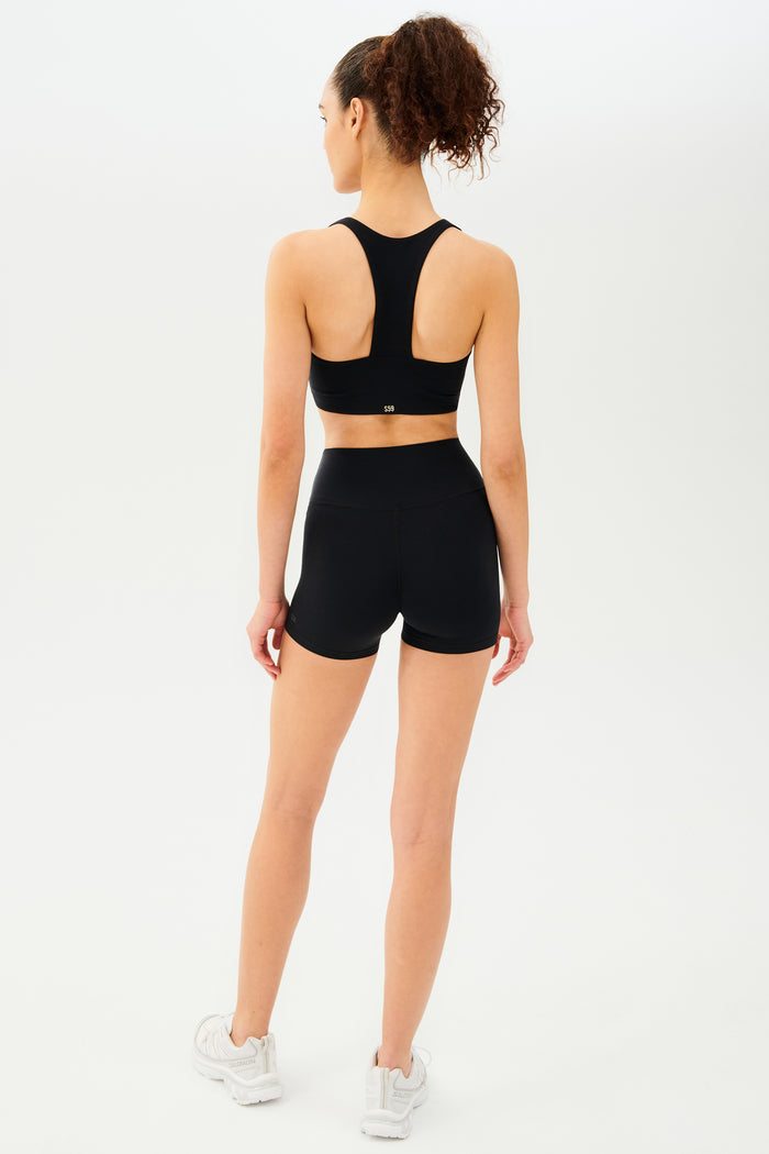 Full back view of girl wearing black shorts with black sports bra and white shoes