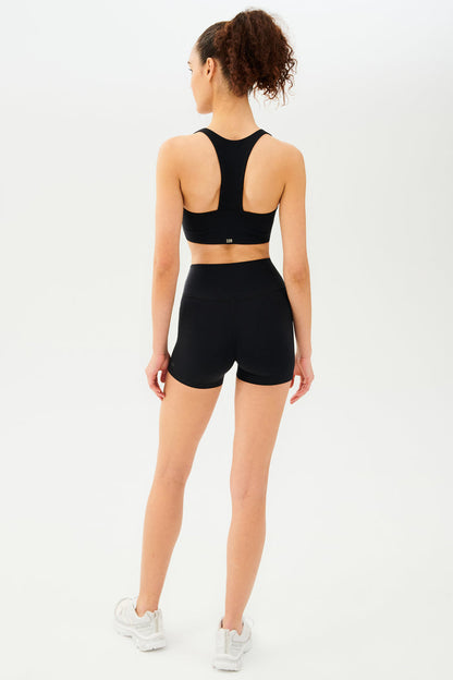 Full back view of girl wearing black shorts with black sports bra and white shoes