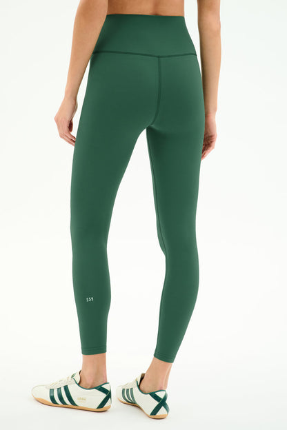 A person is seen from the back wearing SPLITS59 Airweight High Waist Legging in Arugula and white sneakers with green stripes, standing against a plain white background—ideal for hot yoga sessions.