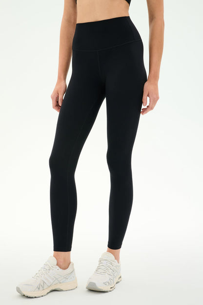 A person wearing SPLITS59 Airweight High Waist Legging in black and white sneakers stands against a plain light background—perfect for hot yoga or all-day comfort thanks to the soft Airweight fabric.