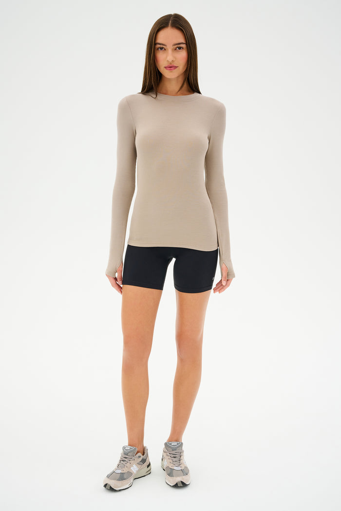 A person in a beige long-sleeve top, SPLITS59 Airweight High Waist Short in black, and gray sneakers stands against a white background.