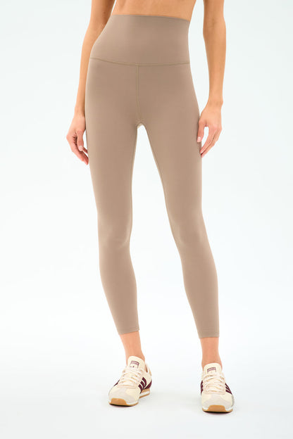 A person wearing SPLITS59 Airweight Super High Waist 7/8 leggings in Latte with cream sneakers, shown midriff to feet against a plain background—ideal for hot yoga thanks to the ultra luxe Airweight fabric.