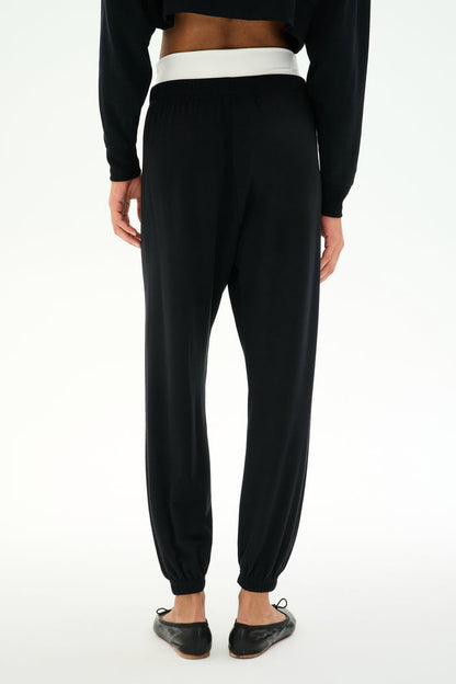 Model wears SPLITS59 Andie Dual Waist Sweatpant - Black/White, featuring a soft modal blend with a contrasting white waistband, paired with black flat shoes, shown from the back against a plain white background.