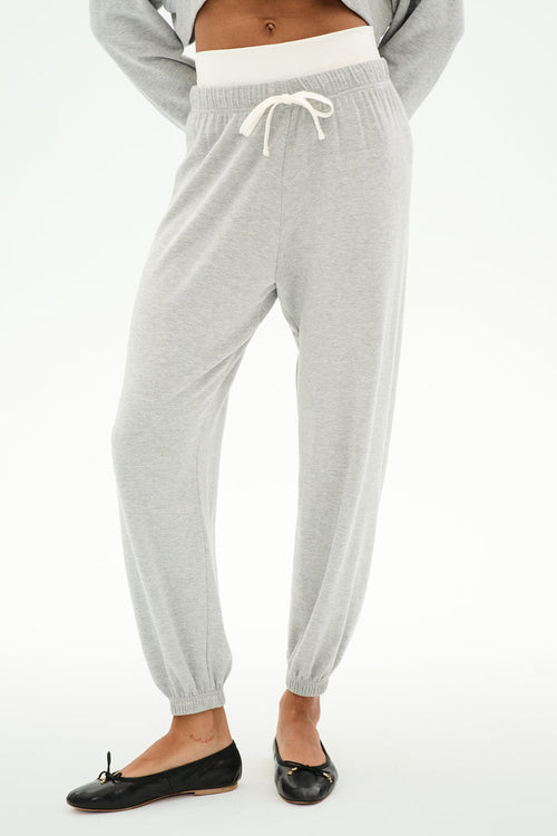 A person wears the SPLITS59 Andie Dual Waist Sweatpant in Heather Grey/White featuring a visible white waistband and white drawstring, paired with black ballet flats, standing against a plain background.