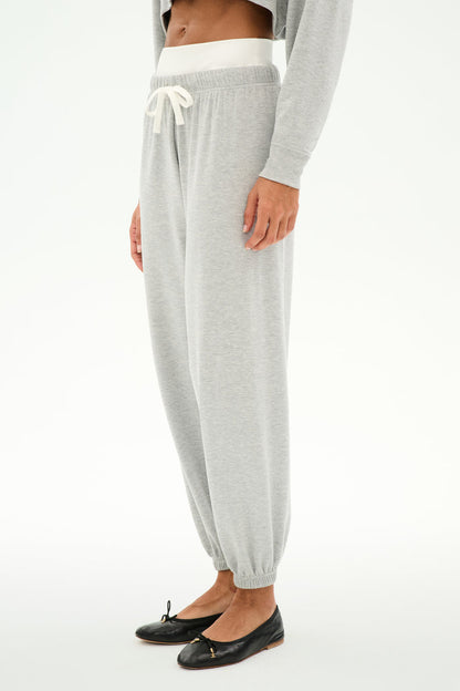 A person wears the SPLITS59 Andie Dual Waist Sweatpant in Heather Grey/White, featuring a white drawstring, paired with a gray top and black ballet flats, standing against a white background.