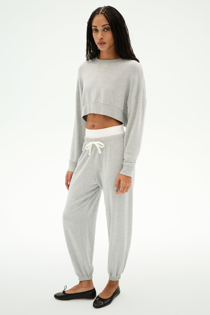 A woman wears SPLITS59’s Andie Dual Waist Sweatpant in Heather Grey/White—a soft, cropped jogger crafted from a modal-spandex blend—paired with black flats, set against a plain white background.
