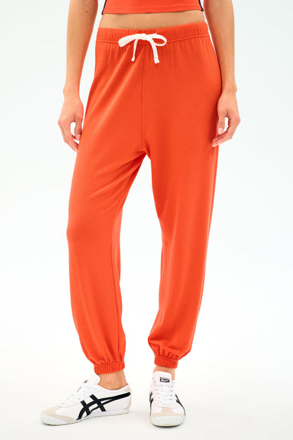 A person wears the SPLITS59 Andie Oversized Fleece Sweatpant in Valencia with a white drawstring and white sneakers, standing against a plain light background.