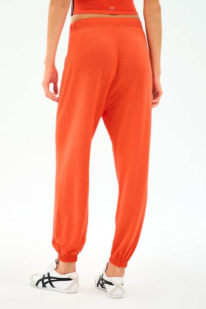 Person wearing SPLITS59 Andie Oversized Fleece Sweatpant - Valencia in bright orange and white athletic shoes, shown from the back against a plain white background.