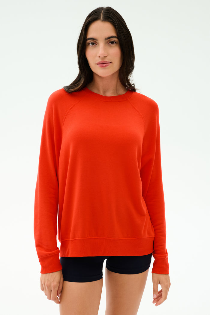 A person with long dark hair wears the SPLITS59 Andie Oversized Fleece Sweatshirt in Lotus Red and black shorts, standing against a plain light background.
