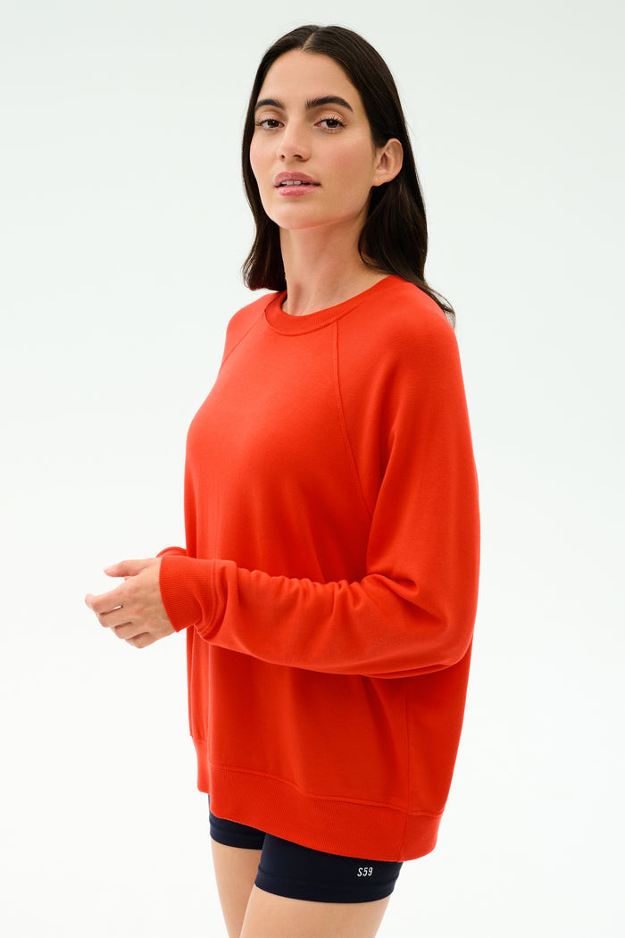 A woman in the SPLITS59 Andie Oversized Fleece Sweatshirt in Lotus Red and black shorts, made in Los Angeles, stands against a light background, facing the camera.