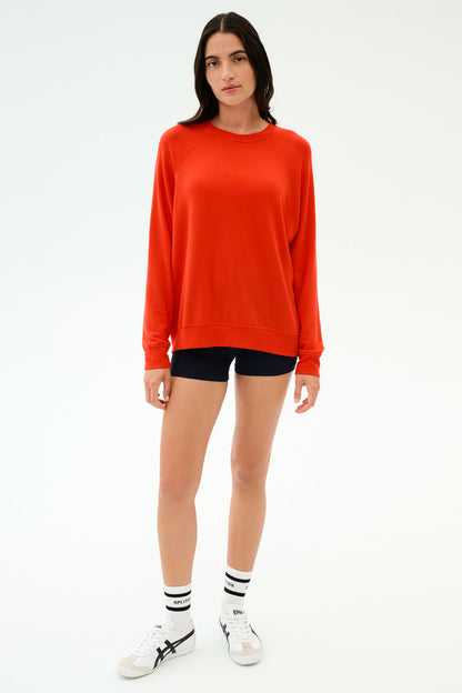 A person stands facing forward in the SPLITS59 Andie Oversized Fleece Sweatshirt in Lotus Red, black shorts, white socks with black stripes, and white sneakers against a plain white background. Made in Los Angeles for all-day comfort.