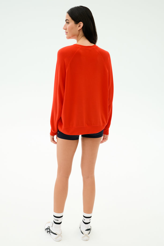 Person stands with their back to the camera in the SPLITS59 Andie Oversized Fleece Sweatshirt in Lotus Red, paired with black shorts and white sneakers. Made in Los Angeles for comfort and style against a plain white background.