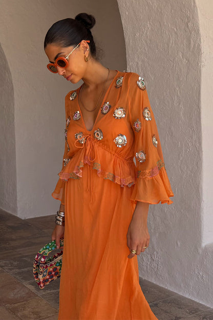 Apricot Embellished Ines Dress in orange with mirror detailing and a peplum hem, styled in a stone archway.