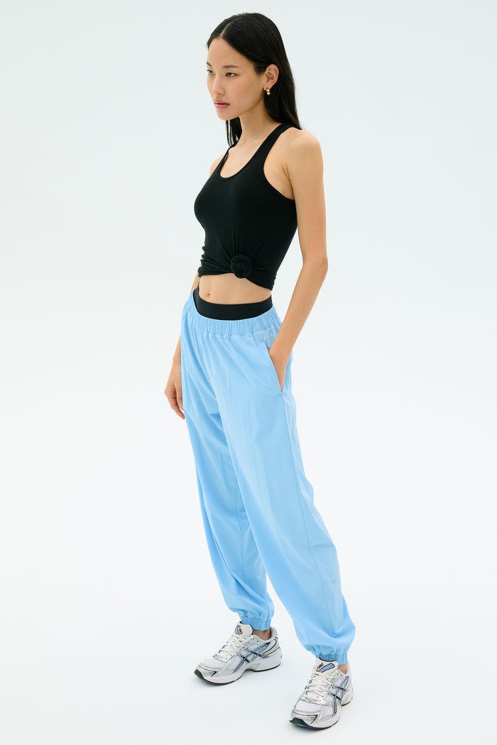 A woman poses against a plain background wearing the Splits59 Ashby Rib Tank in black, paired with light blue joggers and white sneakers—ideal for gym sessions or casual outings.