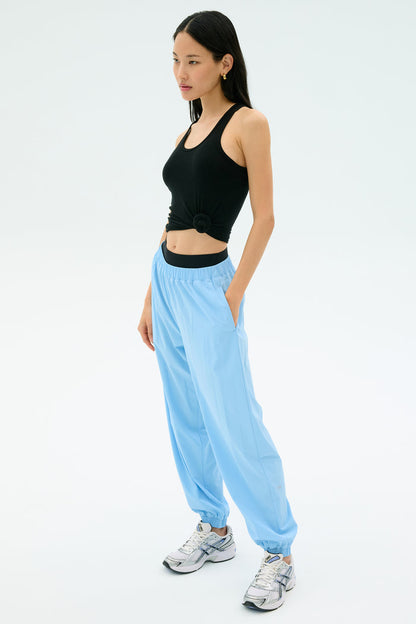 A woman poses against a plain background wearing the Splits59 Ashby Rib Tank in black, paired with light blue joggers and white sneakers—ideal for gym sessions or casual outings.