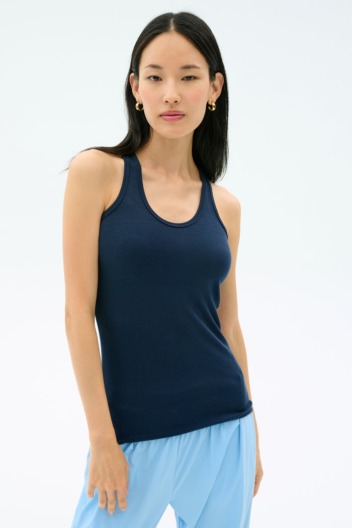 A woman wearing the SPLITS59 Ashby Rib Tank in Indigo and light blue pants stands against a plain light background, facing the camera.
