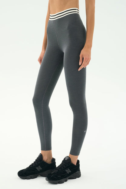 A person wears the SPLITS59 Bailey Active Rib High Waist 7/8 leggings in heather grey with a white-striped waistband and black sneakers, perfect for gym workouts, standing against a plain light background.