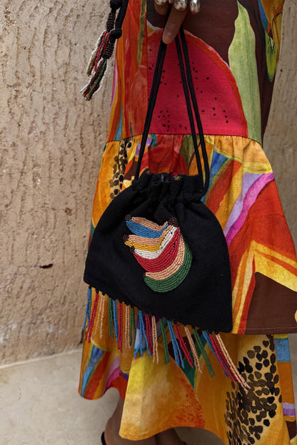 Black Banana Pouch Bag with a beaded motif and multicolour fringe, held over a vibrant fruit-print summer dress.