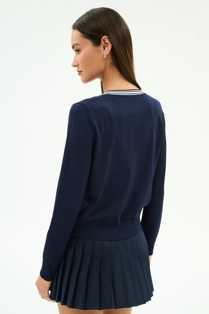 A woman with long brown hair, wearing the SPLITS59 Bekah Knit Cardigan in Indigo/White, stands turned slightly to the side against a plain light background.