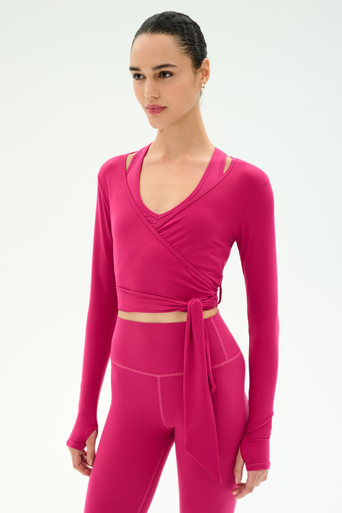 A woman wears the SPLITS59 Bella Airweight Lite Wrap in Sangria with matching high-waisted leggings, standing against a plain light background.