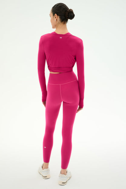 A person stands facing away, wearing the SPLITS59 Bella Airweight Lite Wrap in Sangria with matching high-waisted leggings and white sneakers against a plain white background.