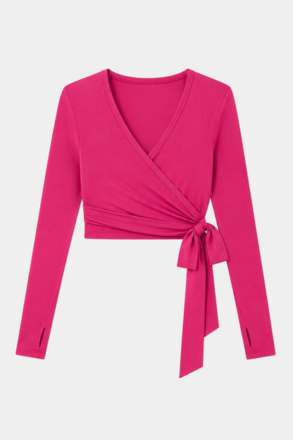 The SPLITS59 Bella Airweight Lite Wrap in Sangria is a long-sleeve, bright pink crop top with a V-neck and side tie, crafted from a soft nylon-spandex blend and shown on a plain white background.