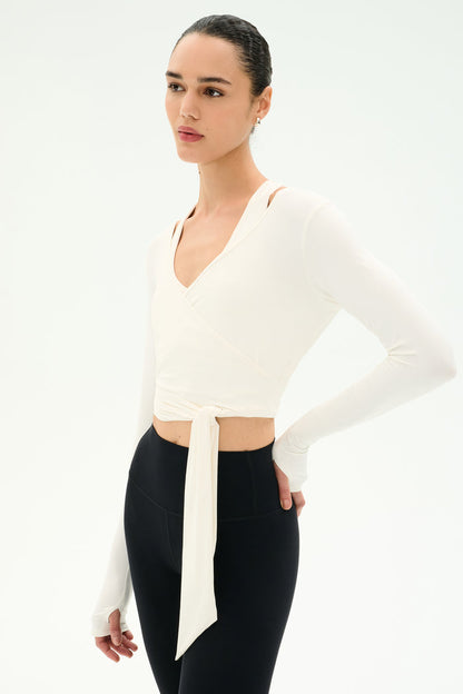 A person wearing the SPLITS59 Bella Airweight Lite Wrap in white stands against a plain white background, paired with black high-waisted nylon-spandex leggings.