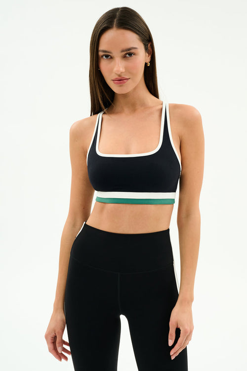 A woman stands against a plain background wearing the SPLITS59 Bianca Rigor Bra in Black/White and high-waisted black spandex leggings.