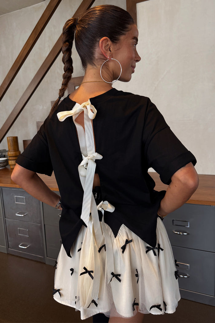 Black Bow Back T-Shirt with cream ribbon fastenings on the open back, shown in a relaxed fit.