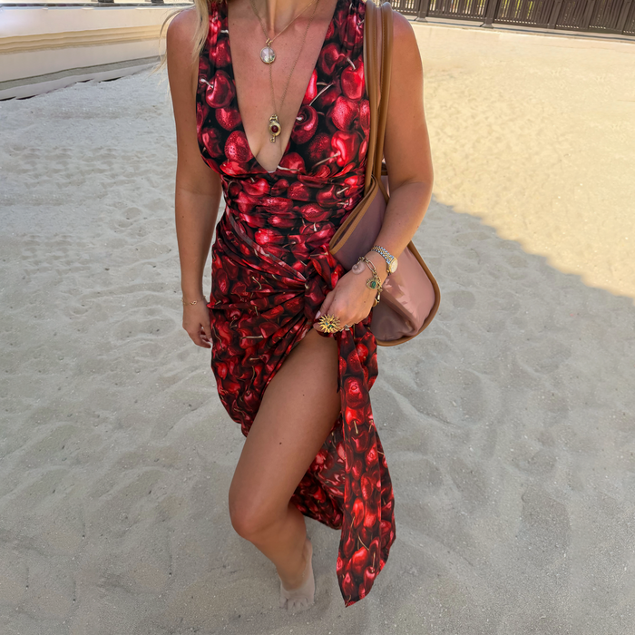 Black Cherry Sarong with an all-over red cherry motif and tie waist, styled on a beach for a vacation look.
