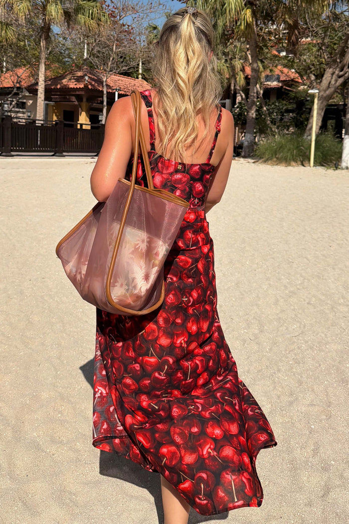 Black Cherry Sarong with a red cherry print and wrap tie waist, worn by a model on a sandy beach vacation.