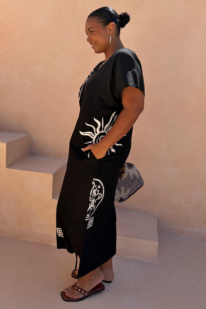 Black Dolce Vita cotton maxi dress with white sun motifs and side pockets, highlighting inclusive sizing.