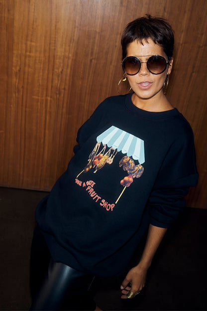 Black Fruit Shop Sweatshirt featuring a colourful fruit stall graphic and relaxed fit, paired with leather-look trousers.