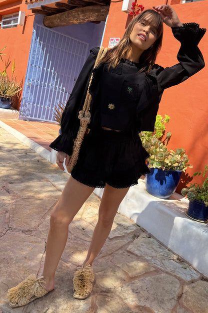 Black Isla top and ruffle shorts co-ord with lace trim and sun embroidery in a sunny outdoor setting.