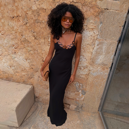 Black Sapna Dress with Ring Detail styled as a maxi dress against a stone wall for a vacation look.