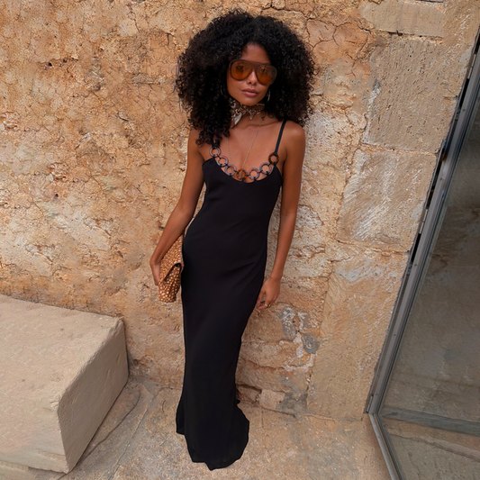 Black Sapna Dress with Ring Detail styled as a maxi dress against a stone wall for a vacation look.