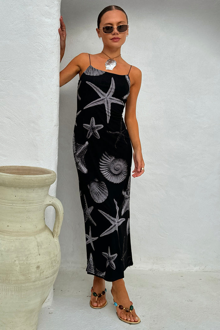 Black Seashell Mesh Cami Dress featuring a white starfish and shell print, styled on a model against a white wall.