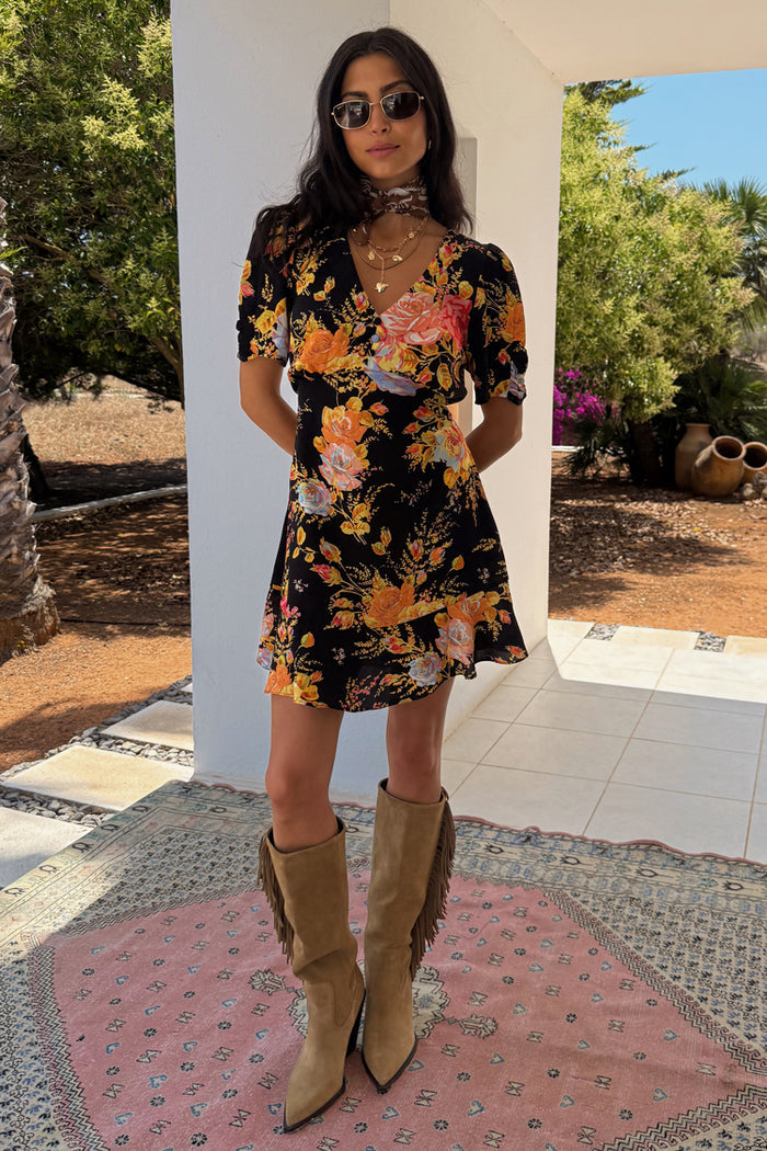 Black Sofia Mini Tea Dress with an intricate floral print and frill hem, styled with tan fringe boots for a vacation look.