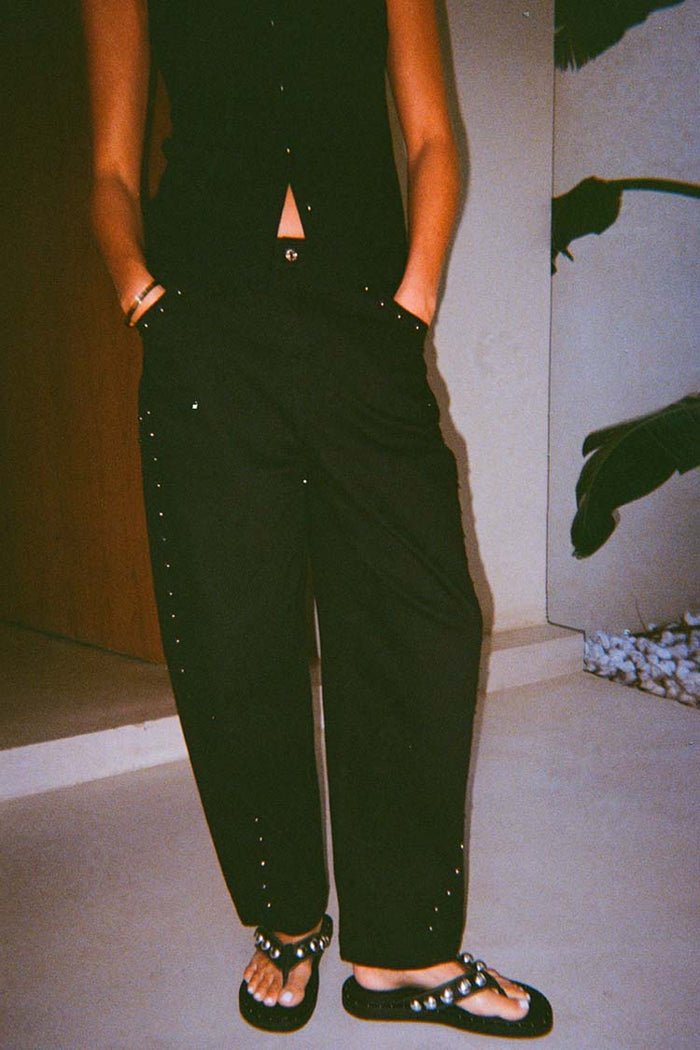 Black barrel leg jeans featuring silver stud detailing along the sides and pockets, shown in a lifestyle shot.