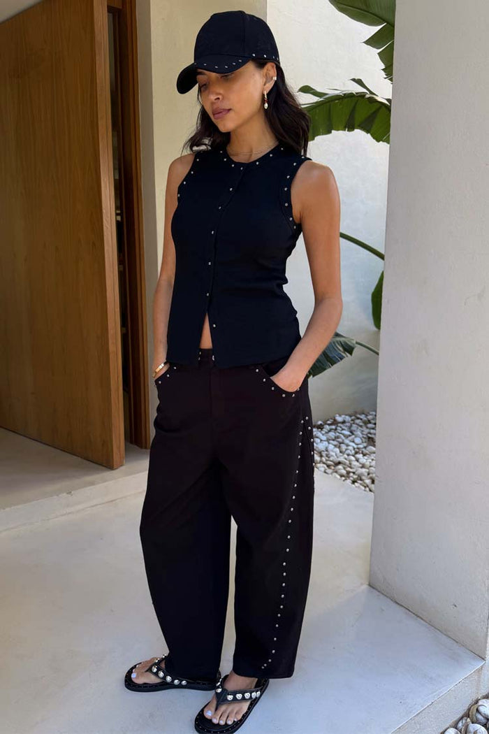 Black Studded Barrel Jeans with side stud details, styled with a sleeveless top and cap on a model.