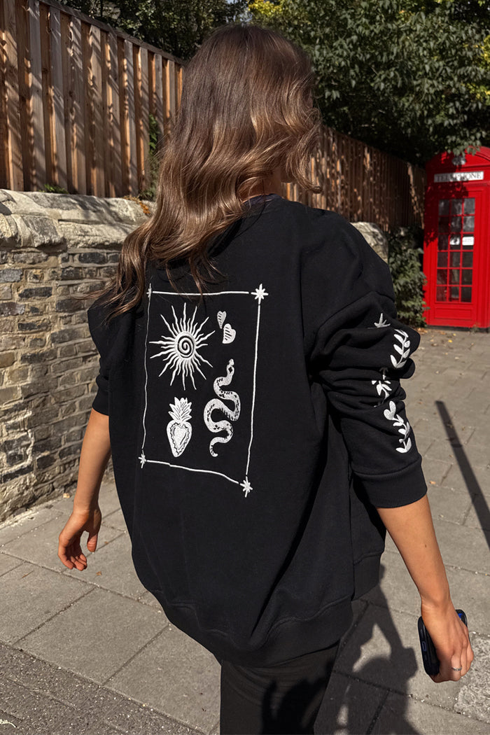 Oversized black sweatshirt with ecru sun and snake embroidery, styled in a London setting with a red phone box.