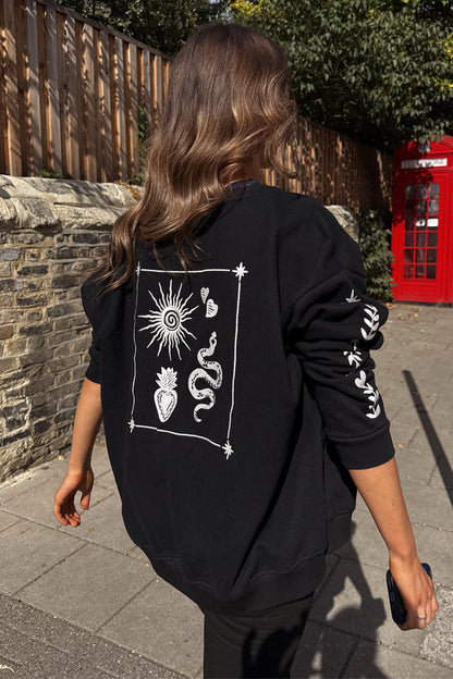 Oversized black sweatshirt with ecru sun and snake embroidery, styled in a London setting with a red phone box.