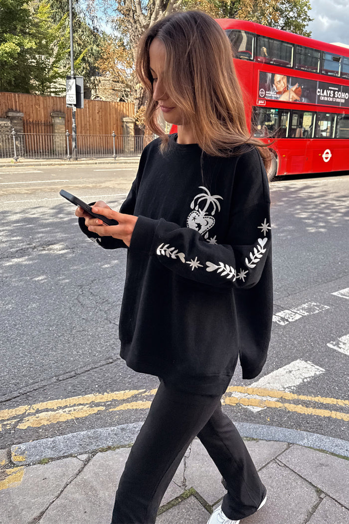 Black oversized sweatshirt with ecru embroidery, styled in a London street setting with a red double-decker bus.