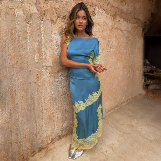Blue and Lemon Millie Skirt and one-shoulder top co-ord with lace trim, leaning against a stone wall.