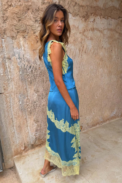 Blue satin Millie Skirt with lemon lace detailing and an asymmetric hem, styled as a co-ord against a rustic wall.