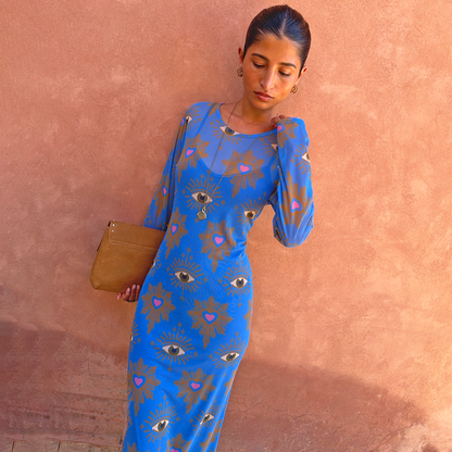 Blue Eye Mesh Dress with eye and heart motifs, a long-sleeved fitted maxi silhouette and tan clutch for vacation.