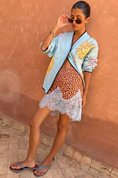 Blue Mystical jacquard cardigan featuring sun and moon motifs and brown trims, styled with a patterned lace-trim skirt.